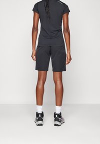 Czarna koszulka sportowa z krótkimi rękawami i pasujące czarne szorty, w połączeniu z szaro-czarnymi butami sportowymi i białymi skarpetkami do kostek.