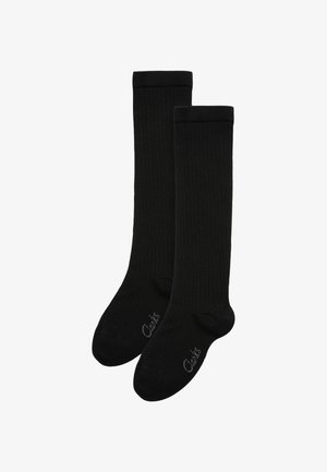 Fekete bordázott, térdig érő zoknik, puha anyagból, megerősített orral és sarokkal. Márkajelzés a talpon látható.