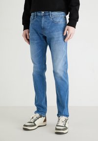 Light blue denim jeans with a straight fit, five pockets, and subtle fading. Paired with white sneakers featuring gray and brown accents.