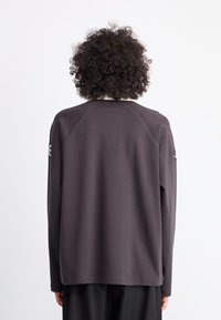 Mørkegrå langærmet sweatshirt med rund hals og raglanærmer. Har en glat tekstur og et diskret logo på overarmen.