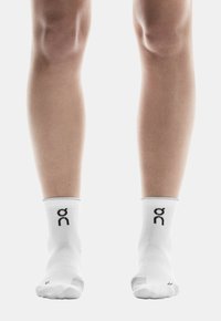 Weisse Knöchel-socken mit einem schwarzen Logo am Bündchen, einer gerippten Textur und einem engen Sitz um die Füße und Beine.