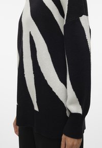 Pullover a righe bianche e nere realizzato in un tessuto morbido, con vestibilità ampia, maniche lunghe e orlo a coste. I dettagli includono audaci motivi a zigzag.