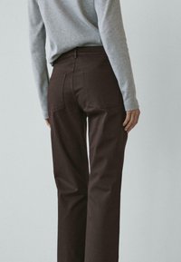 Tmavě hnědé kalhoty s vysokým pasem a rovnými nohavicemi, vybavené zadními kapsami a hladkou texturou látky, doplněné šedým dlouhým rukávem trička.