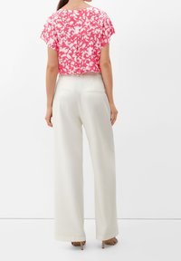 Top rosa tagliato con un motivo floreale e maniche a campana, abbinato a pantaloni bianchi a gamba larga e sandali con tacco beige.