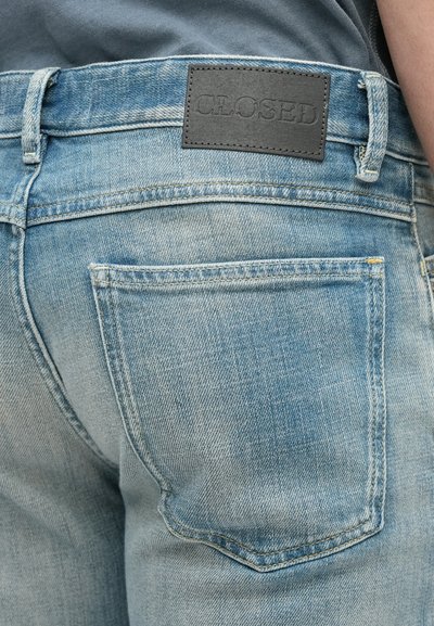 Φωτεινά μπλε τζιν με ξεθωριασμένη υφή, με μαύρη δερμάτινη ετικέτα με την επιγραφή "CLOSED" στη μέση και λεπτομέρεια σε πίσω τσέπη.