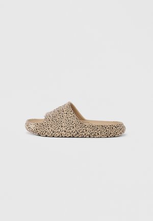 Slip-on-sandaal beeži tallaga ja lai rihmaga, millel on musta leopardimustri kujundus, nähtav küljelt üksikasjalikul taustal.