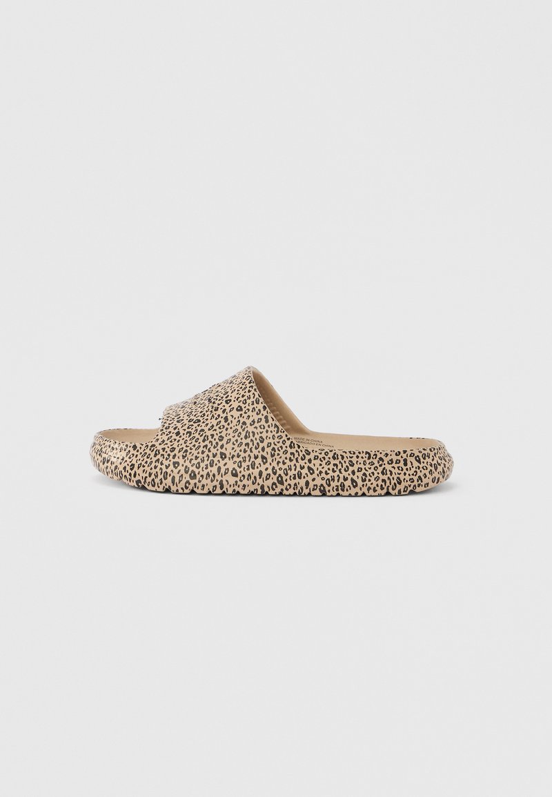 Παντόφλα χωρίς λουράκι με μπεζ σόλα και φαρδιά λουρά με μοτίβο μαύρης λεοπάρδαλης, απεικονίζεται από το πλάι σε μονόχρωμο φόντο.