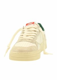Sneaker in suede crema e beige con punta forata, dettagli marroni, design con lacci e interno verde. Etichetta rossa con logo sulla linguetta.