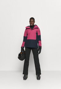 Helles rosa und marineblaues Pullover-Jacke mit Reißverschluss, Kapuze und Seitentaschen. Schwarze Hose und Handschuhe, hält einen schwarzen Helm. Schneestiefel inklusive.