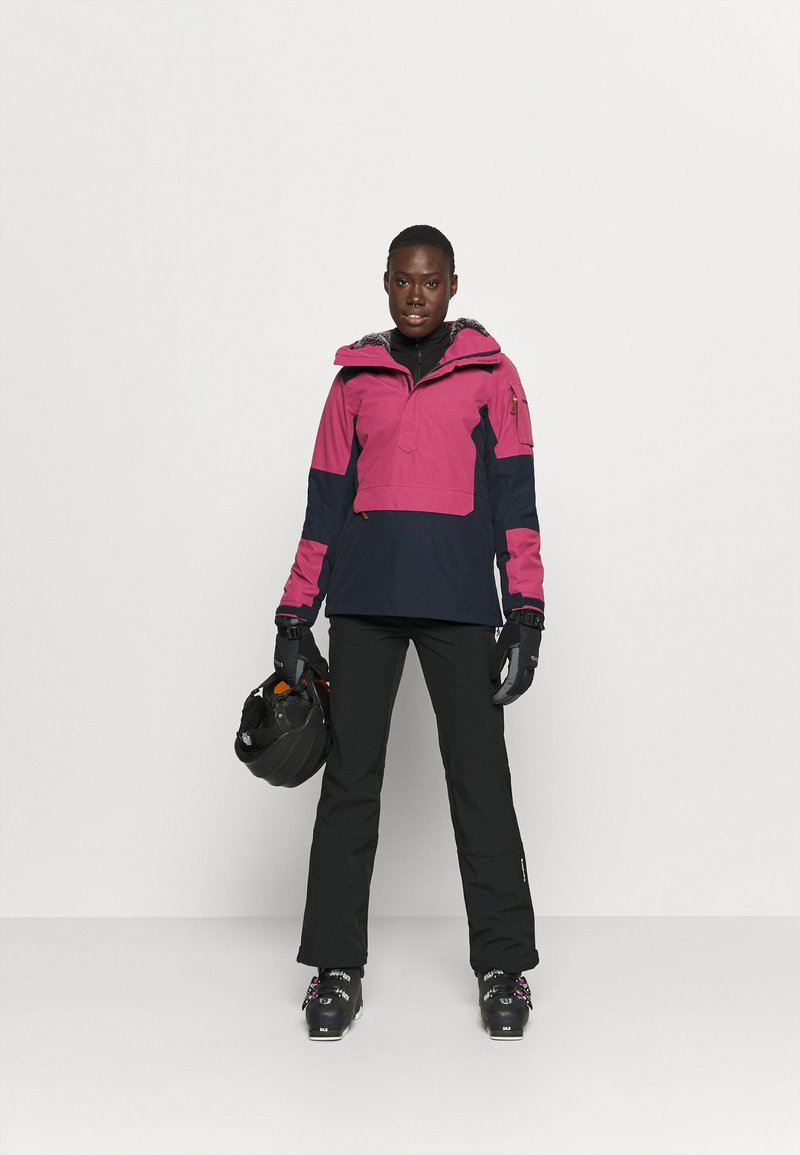 Jasnoróżowa i granatowa bluza z zamkiem błyskawicznym, kapturem i bocznymi kieszeniami. Czarne spodnie i rękawiczki, trzymając czarny kask. W skład zestawu wchodzą również śniegowce.