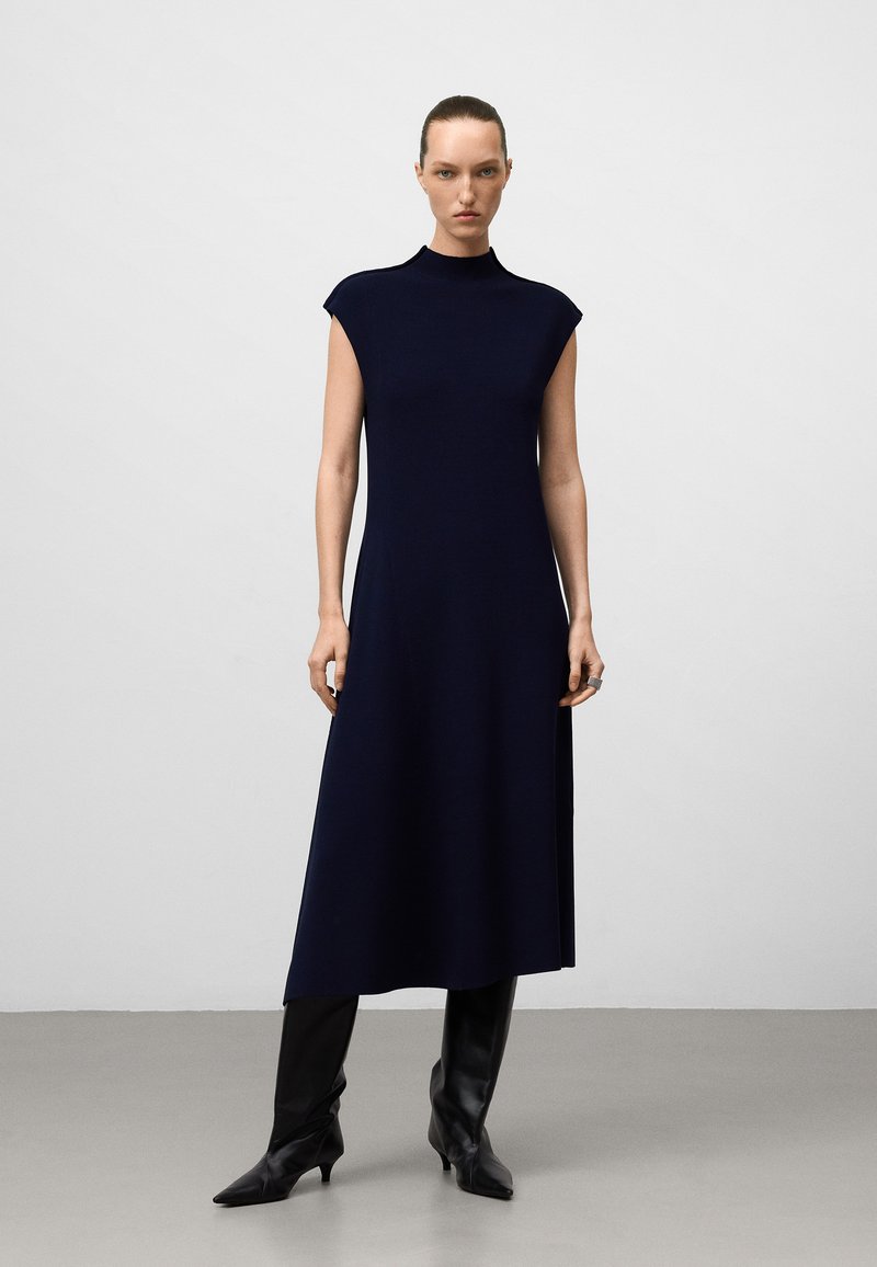Abito midi senza maniche di color navy con collo alto, realizzato in un tessuto testurizzato, caratterizzato da una vestibilità rilassata e che arriva fino a metà polpaccio.