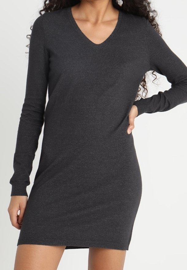 Femme portant une robe-pull cintrée à manches longues, col en V, de couleur gris foncé, debout avec une main sur la hanche.