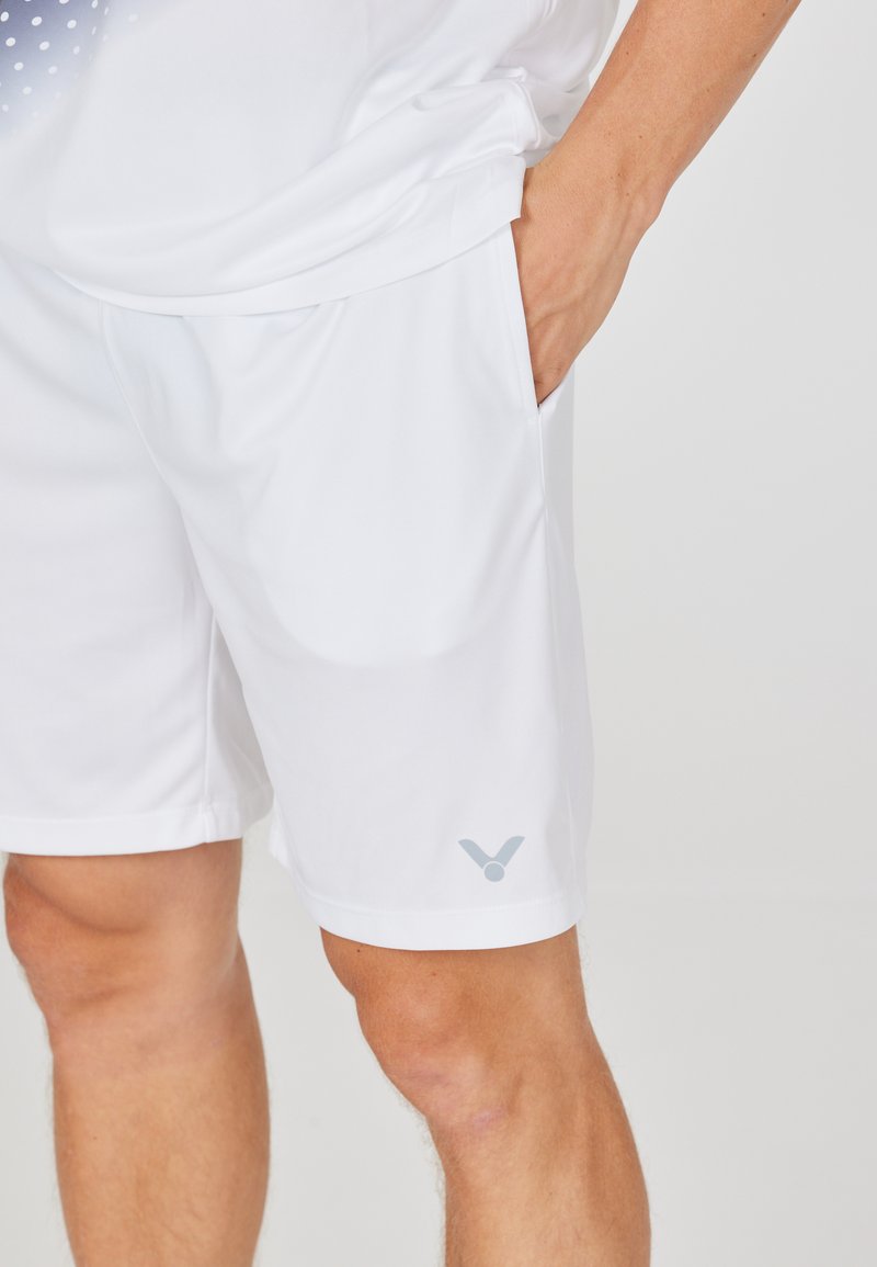 Hvide atletiske shorts lavet af letvægtsstof, med en glat tekstur, sidelommer og et diskret gråt logo ved kanten.