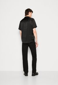 Maglietta nera a maniche corte con righe verticali, realizzata in un tessuto liscio e leggero. Abbinata a pantaloni neri a gamba dritta e scarpe nere.