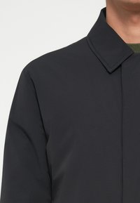 Σκούρο ναυτικό σακάκι με δομημένο κολάρο, λεία υφή και ελάχιστο σχεδιασμό με λεπτές ραφές.