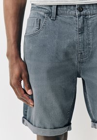 Graue Jeansshorts aus Denim mit umgeschlagenem Saum, vordere Tasche und Knopfverschluss. Glatte Textur mit dezenten Verblassungsdetails.