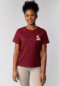 Burgunderfarbene Baumwoll-T-Shirt mit einem Corgi-Motiv auf der Brust. Kurze Ärmel, Rundhalsausschnitt, lockere Passform. Kombiniert mit beigen Rippleggings.