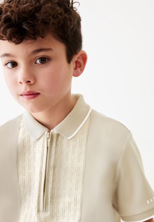 Beige polo shirt med tekstureret panel, lynlås ved halsen og hvide krave accenter. Korte ærmer med mærkedetail på højre side.
