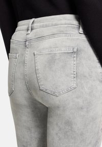 Jasnoszare dżinsy z lekko wyblakłą fakturą. Dwie tylne kieszenie z widocznym szwem, wysoka talia i brak widocznych elementów metalowych.