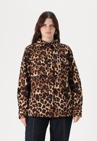 Giacca in stampa leopardata con macchie marroni e nere su uno sfondo beige, due tasche sul petto e colletto. Tessuto morbido.