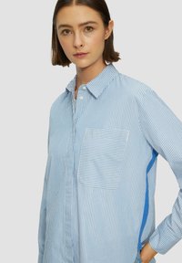 Blauw en wit gestreepte overhemden met knopen, met een zak, voorzien van een effen blauwe accent aan de zijkant. Gemaakt van een lichtgewicht stof.