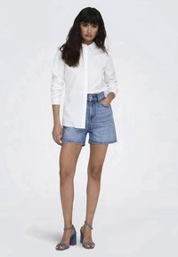 Witte blouse, hoge taille spijkerbroekshorts, blauwe haksandalen. Gladde stof, standaard pasvorm, licht gewassen denim, niet verstoord ontwerp.