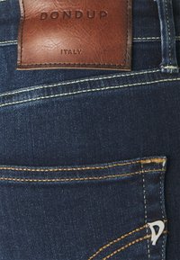 Dark blue denim jeans with defined stitching, a brown leather label reading "DON DUP," and a silver accent on the front pocket.