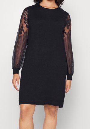 Czarna sukienka z długimi, przezroczystymi koronkowymi rękawami i prążkowanymi mankietami. Główna część wykonana jest z gładkiego materiału, posiada okrągły dekolt i prosty krój.