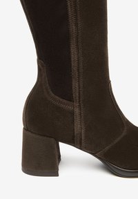 Stivale in suede marrone con tacco a blocco, texture morbida, pannelli laterali e dettagli di cucitura lungo le cuciture.