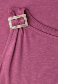 Tissu rose doux avec une boucle rectangulaire beige fixant un détail de sangle froncée sur un vêtement.