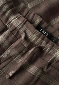 Pantalones a cuadros marrón con una tela suave y texturizada, cinturilla elástica y cordón. Etiqueta visible con la marca "LMTD."