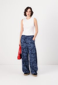 Pantalons larges à motif floral marine avec taille élastique, associés à un haut sans manches blanc et un sac à main rouge. Chaussures noires et beiges.