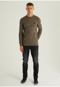 Braun gestricktes Langarmshirt mit strukturiertem Muster, Rundhalsausschnitt und kleinem Logo-Patch auf der Brust.