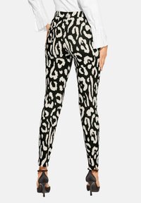 Schwarz-weiße Leggings mit Leopardenmuster in taillierter Form, aus glattem Stoff gefertigt, kombiniert mit schwarzen High Heels.