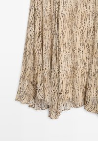 Beige Stoffrock mit einem wellenförmigen Muster aus dunkelbraunen Punkten, leichtem Material und fließendem Design mit einer gewellten Saumlänge.