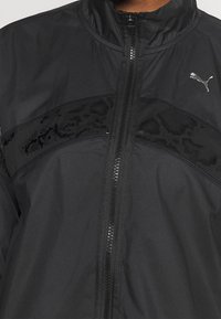 Schwarze Sportjacke mit Stehkragen, Frontreißverschluss und strukturiertem schwarzen Einsatz mit einem dezenten Leopardenmuster über der Brust.