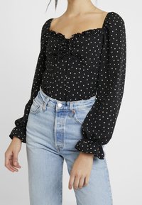 Mustat pusero, jossa on liehukkeet hihassa, röyhelökaulus ja edessä kiristettävä nyöri. Valkoinen tähtikuosi tuo lisäyksityiskohtia. Yhdistetty vaaleansinihin farkkuihin.