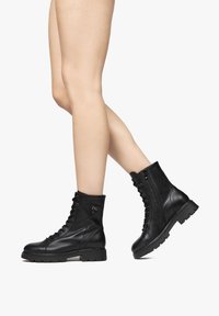 Zwarte leren enkelboots met een vetersluiting aan de voorkant en een rits aan de zijkant, voorzien van een chunky zool en logo-detail aan de zijkant. Textuurafwerking.