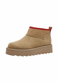 Beige mokkanahkasaappaat, joissa on pyöreä nenä, punaiset elastiset reunukset ja viistopohja, jossa on sahalaitakuviot.