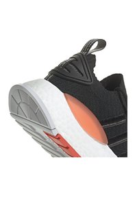 Sneaker nera in maglia con suola testurizzata bianca, supporto al tallone arancione e dettagli in gomma grigia sulla suola. Include una linguetta per il trasporto.