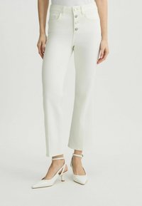 Jeans a vita alta, di colore bianco sporco, a campana con chiusura a cinque bottoni e due tasche frontali, abbinati a tacchi slingback bianchi.