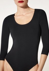 Body nero a maniche lunghe con scollatura a barco, realizzato in tessuto liscio. Presenta un design aderente e aperture per le gambe a vita alta.