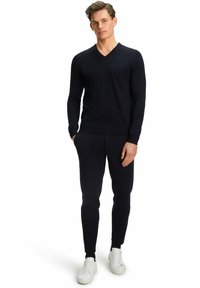 Navy V-Ausschnitt-Pullover mit langen Ärmeln, kombiniert mit schmal geschnittenen navy Jogginghosen und weißen Sneakers. Glatte Textur, lässiges Design, minimale Details.