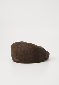 Brown wool cap with a textured houndstooth pattern, featuring a rounded shape and a small, branded leather tag on the side.