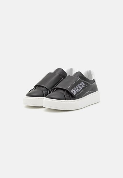 Zapatillas de cuero negras con costuras blancas, que cuentan con una cinta ancha en la parte frontal y una suela de goma blanca texturizada.
