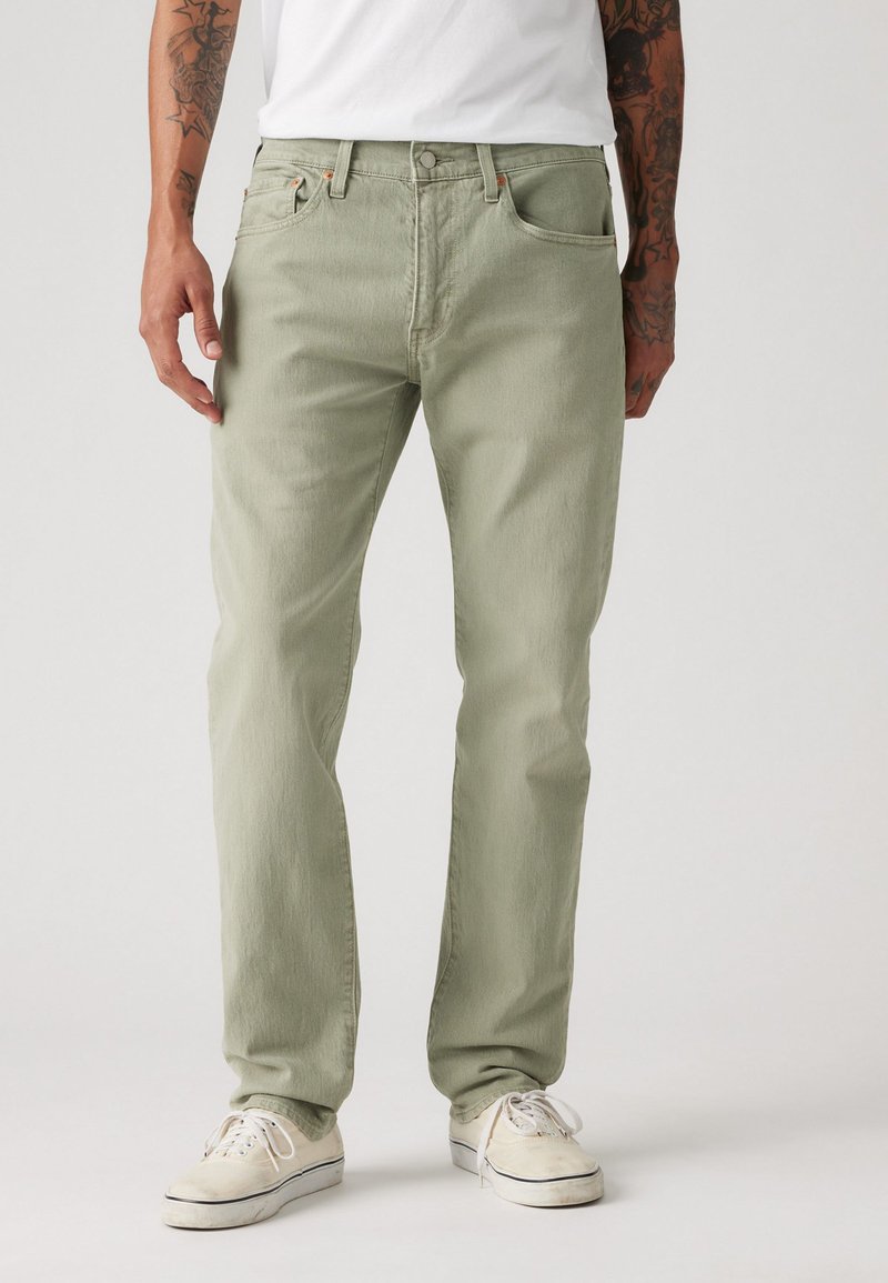 Hellgrüne Baumwolljeans mit einem lässigen Schnitt, mit einem Knopfverschluss, vorderen und hinteren Taschen sowie subtiler Textur. Kombiniert mit weißen Sneakers.