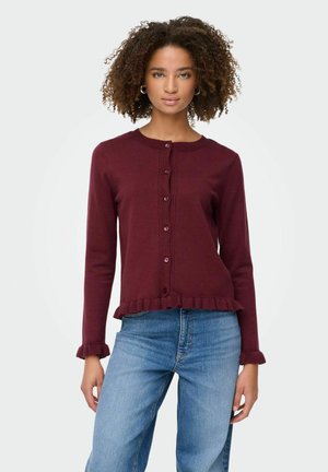 Bordeaux gebreide cardigan met lange mouwen, ronde hals, knopen aan de voorkant en een gerimpelde zoom en manchetten, gecombineerd met blauwe spijkerbroeken.