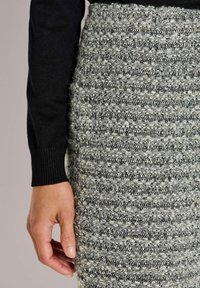 Ein schwarzer, gestrickter Pullover, kombiniert mit einem strukturierten, grau-weißen Rock mit einem Muster aus horizontalen Streifen und einer weichen, flauschigen Optik.