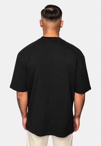 Sort oversized t-shirt med korte ærmer, rund hals og en glat stofstruktur. Vist fra bagsiden, hvilket afslører et minimalistisk design.