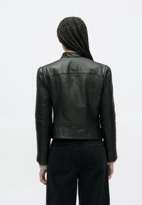 Czarna skórzana kurtka z żebrowanymi detalami na ramionach i rękawach, krótki krój oraz gładka tekstura. Noszona z ciemnymi dżinsami, widok od tyłu.